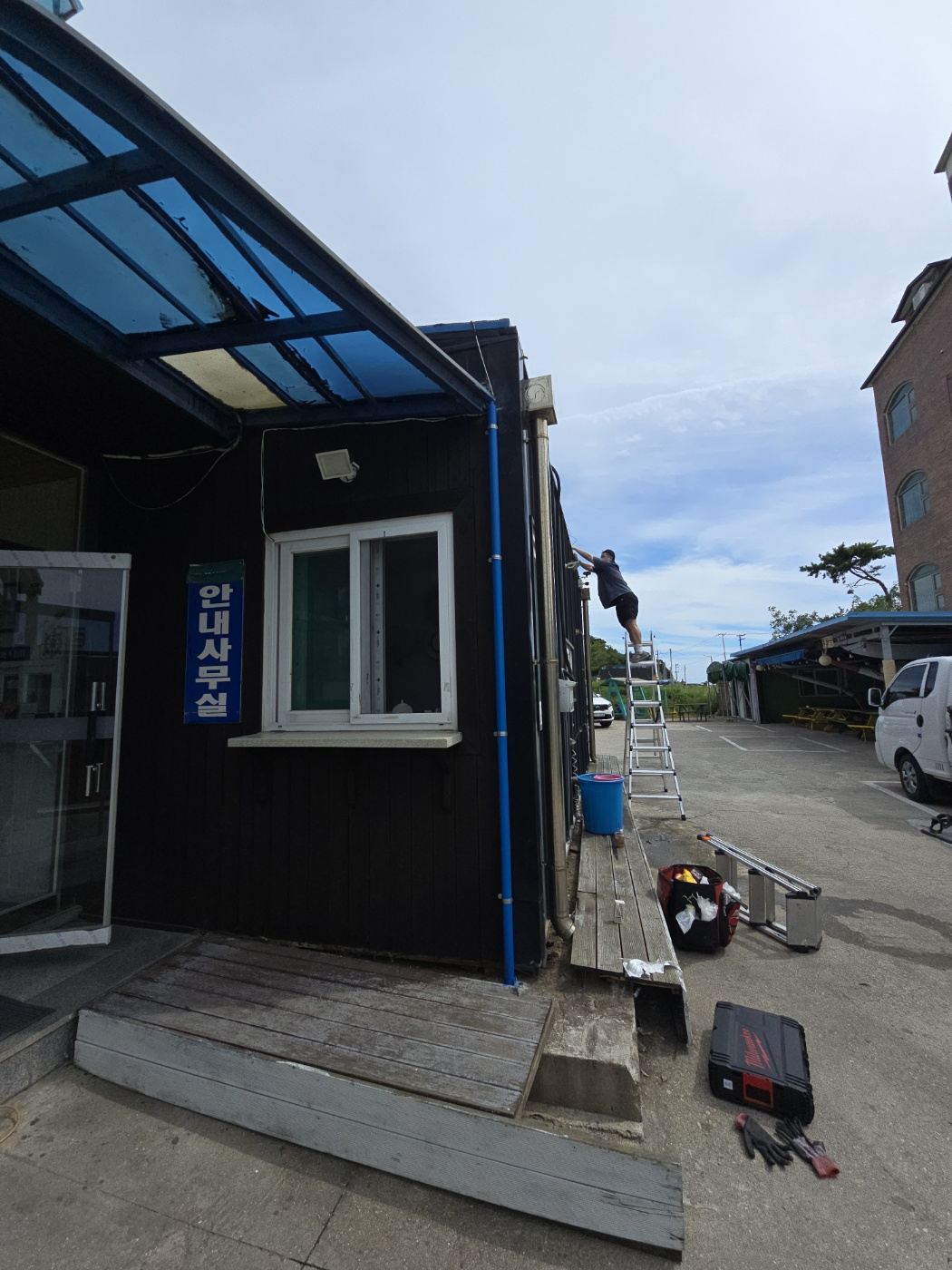 캐노피 상부 홈통 보수를 위해 사다리를 세우고 작업하는 모습